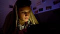 Tired teenager surfing internet on tab instead of sleeping, lying under blanket