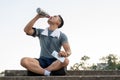 Tired and thirsty Asian man in sportswear is sitting on the stairs and drinking water from a bottle Royalty Free Stock Photo