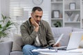 Tired and thoughtful african american man working from home on laptop with documents and bills. Overtime over the Royalty Free Stock Photo