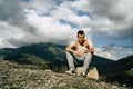 Tired traveling man resting on hill. Exhausted male tourist sitting on stone after active trekking in mountains