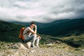 Tired traveling man resting on hill. Exhausted male tourist sitting on stone after active trekking in mountains