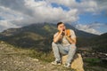 Tired traveling man resting on hill. Exhausted male tourist sitting on stone and sweetly yawning with closed eyes after