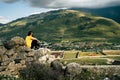 Tired traveling woman resting on hill. Exhausted male tourist sitting on stone after active trekking in mountains