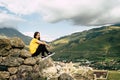 Tired traveling woman resting on hill. Exhausted male tourist sitting on stone after active trekking in mountains