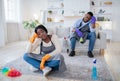 Tired unhappy black woman sitting on floor after home cleanup, her boyfriend sleeping on couch, indoors Royalty Free Stock Photo