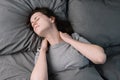 Tired unhappy young woman lying in bed in morning feels pain in neck after night sleep, massage tense neck muscles Royalty Free Stock Photo