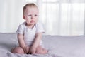 Tired and upset baby boy. Calm infant kid sitting on the bed across from the window. Copy space