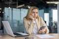 A tired, upset, disappointed business woman is sitting in the office at the desk, holding the phone in her hand and Royalty Free Stock Photo