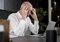 Tired or upset mature businessman sitting at desk and working on laptop. Employee thinking of deadline or workload or