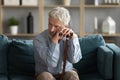 Tired upset mature man holding walking stick, sitting on couch