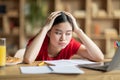 Tired upset teen chinese female hold head with hands, look at laptop in room interior