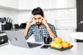 Tired upset young indian man sitting at kitchen table with laptop Royalty Free Stock Photo