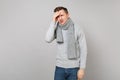 Tired upset young man in gray sweater, scarf having headache, put hand on head on grey wall background. Healthy