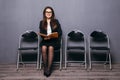 Tired of waiting. Bored young businesswoman holding paper and looking away while sitting on chair against black background Royalty Free Stock Photo