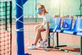 Tired weak girl resting on a plastic chair bench on an outdoor tennis court