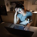 Tired woman in headphones and glasses working overtime over a laptop. Female freelancer working remotely at home in the Royalty Free Stock Photo