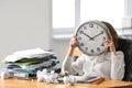 Tired woman hiding face behind clock at table in office. Time management concept Royalty Free Stock Photo