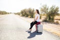 Tired woman hitchhiker with suitcase on road