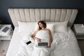 Tired woman with laptop and smartphone sleeping in bed at home, above view Royalty Free Stock Photo