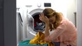 Tired woman loading clothes in washing machine, annoyed with housework routine Royalty Free Stock Photo