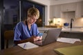 Tired Woman In Medical Scrubs Looking At Mobile Phone Working Or Studying On Laptop At Home At Night Royalty Free Stock Photo