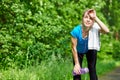 Tired woman runner having rest after running hard on road in forest, bending forward, resting elbows on her knees Royalty Free Stock Photo