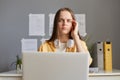 Tired woman sitting in front of computer feeling fatigue suffering headache spending long hours doing online work holding laptop Royalty Free Stock Photo