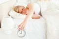 Tired woman switching off her alarm clock