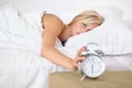 Tired, woman and wake up with alarm in morning and sleeping on bed in home with stress or fatigue. Press, snooze and Royalty Free Stock Photo