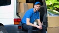 Tired worker of moving company resting, sitting in van full of cardboard boxes