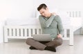 Tired young Asian handsome man massaging aching neck suffering from ache while sitting on the floor working laptop in beddroom. Royalty Free Stock Photo