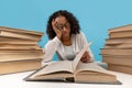 Tired young black female student surrounded by stacks of books reading textbook, getting ready for exam, feeling bored Royalty Free Stock Photo