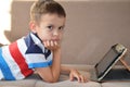 Tired young boy with glasses sitting and holding his head on the tablet in front of the computer, tablet and laptop Royalty Free Stock Photo