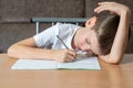 Tired young boy lay down on a desk writing down homework or preparing for an exam, front view Royalty Free Stock Photo