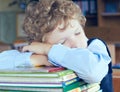 Tired young boy sitting and sleeping at the table with his head and hands on the books. Hard studying. Royalty Free Stock Photo