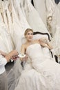 Tired young bride in wedding dress sitting while mother showing footwear