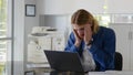 Tired young businessman feeling stressed and overwhelmed sitting in modern office with laptop Royalty Free Stock Photo