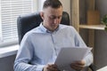 Tired young director of company with documents in his own office. Successful man in leather chair. Checking of reports Royalty Free Stock Photo