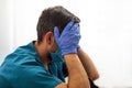 Tired young doctor from lack of sleep sits near the window covering his face with his hands Royalty Free Stock Photo