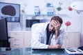 Tired young doctor trying to focus holding his head sitting down in the office Royalty Free Stock Photo