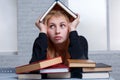 Tired girl , sits next to a pile of books and holds the book over head. Learning concept. Royalty Free Stock Photo
