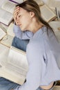 A tired young girl sits among a large pile of opened books. Training and education. Vertical Royalty Free Stock Photo