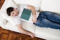 Tired young man sleeping on couch with book on lap Royalty Free Stock Photo