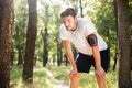 Tired young sportsman standing and relaxing after running in forest