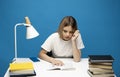 Tired young student woman in white casual clothes sitting at the table reading the book in library of university or Royalty Free Stock Photo