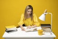 Tired young student woman in yellow casual clothes sitting at the table reading the book in library of university or Royalty Free Stock Photo