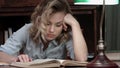 Tired young woman falling asleep over a book while sitting at the table after long day of work Royalty Free Stock Photo