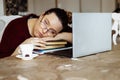 Tired young woman in glasses lying down on books and looking away near laptop at desk in home room. Tiredness from