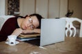 Tired young woman in glasses sleeping on books near laptop at desk in home room. Tiredness from monotonous study and