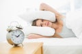 Tired young woman lying in her bed covering her ears with pillow Royalty Free Stock Photo